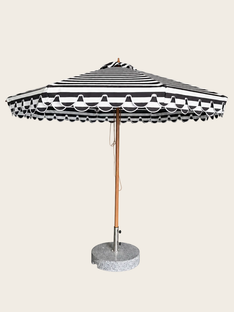 A grey and white striped patio umbrella with a scalloped edge, a wooden pole, and a round concrete base on a white background.