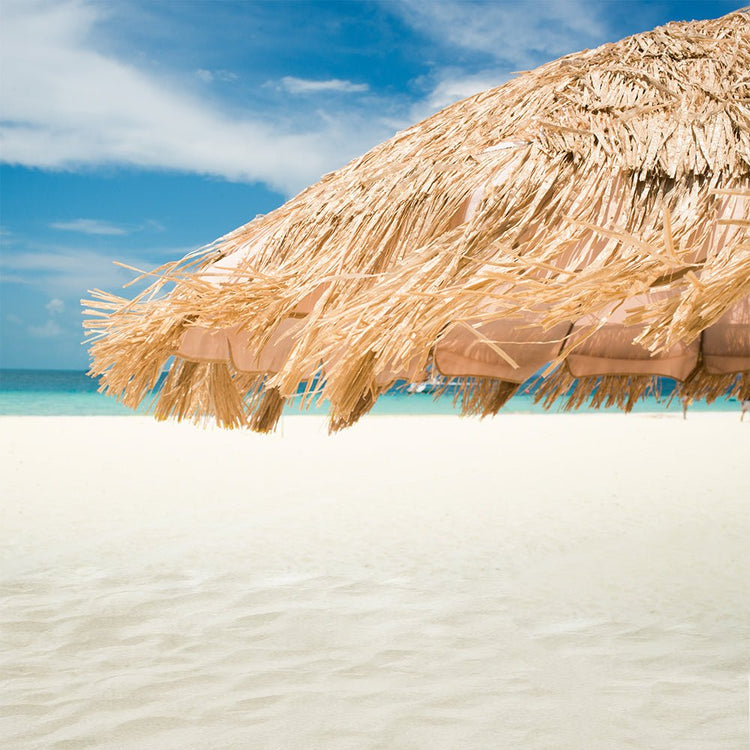 Hula 210cm Beach Umbrella with raffia thatch canopy offering UPF 50+ sun protection and quick-twist sand anchor on a sunny beach